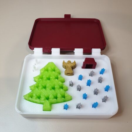 Open Christmas‑in‑a‑Box showing green tree, gold angel topper, red stand, and bluegray star pieces in a white tray.